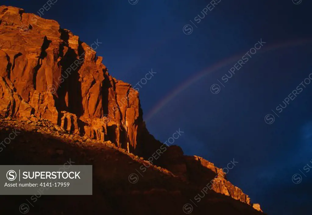 rainbow & storm clouds behind sunlit wingate rock (sandstone) capitol reef national park, utah, mid-western usa spring 