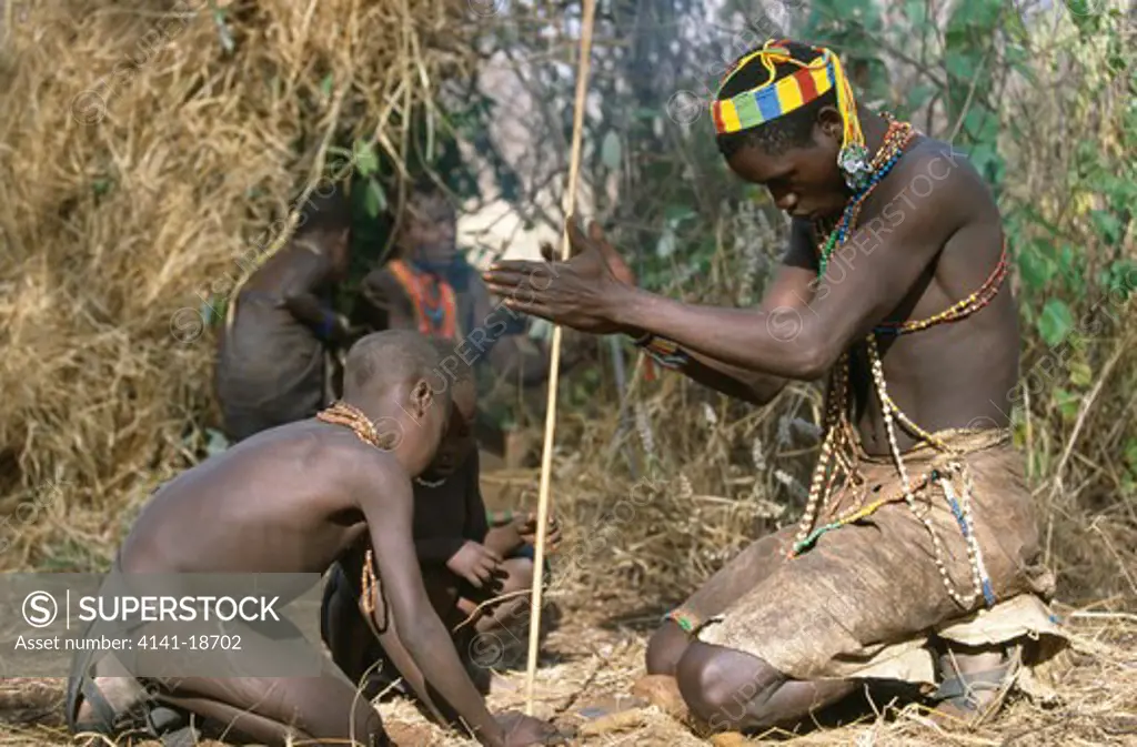 hadzabe man teaching children how to start a fire with a stick lake eyasi area, tanzania