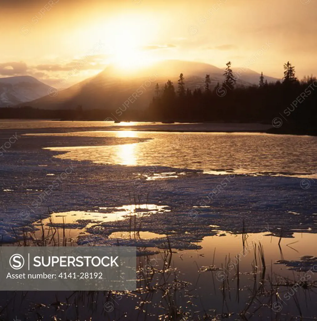 sun shining through rain shower over icy lake & snowy mountains hemsedal, buskerud county, norway june 
