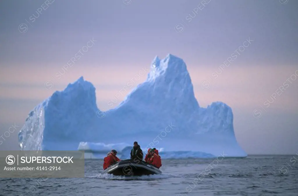 tourists in zodiac dinghy with iceberg in background, antarctica.