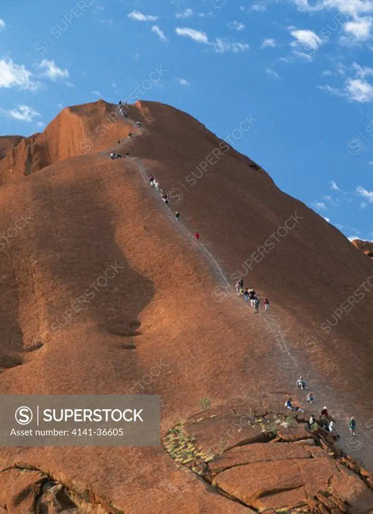 tourists climbing ayers rock uluru national park, northern territory, australia 
