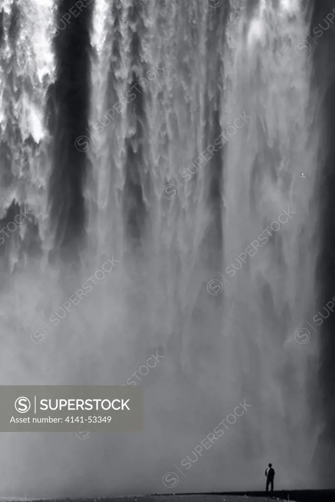 A Man Is Standing In Front Of The Skogafoss Waterfall In Southern Iceland.