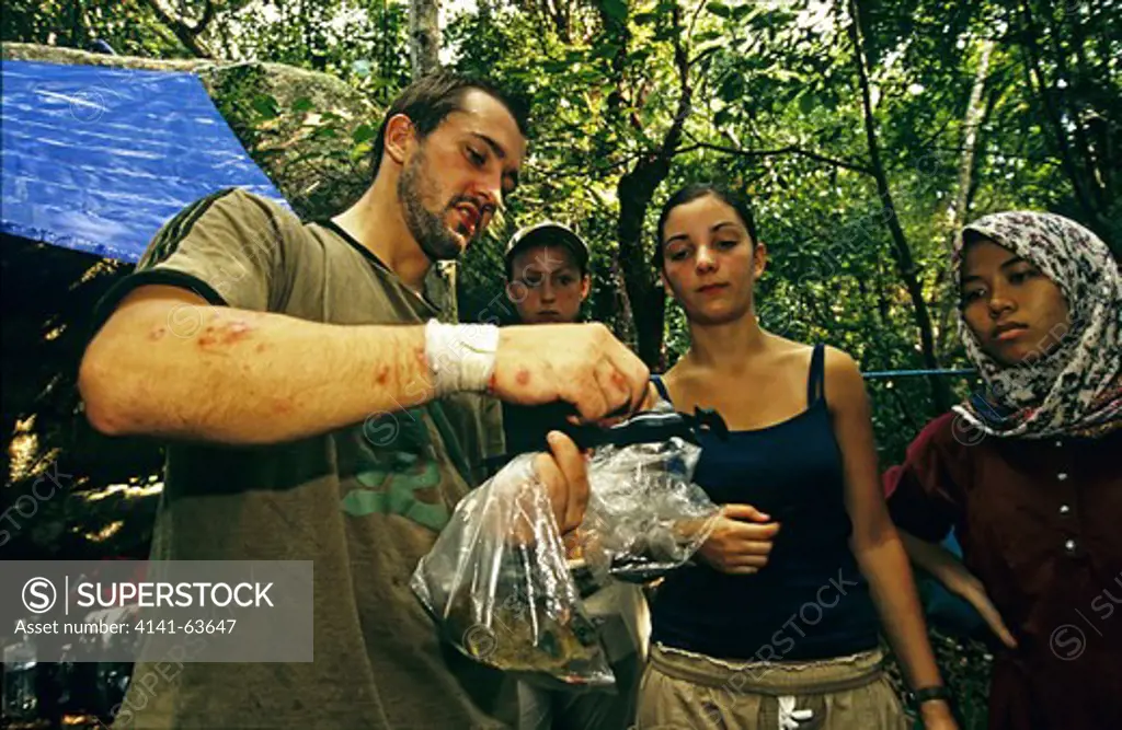 Camp Survival,  People In Rough Rainforest Camp Gather To Look At Captured Rat In A Food Bag And Is Now Potrential Food,  Taman Negara, Malaysia