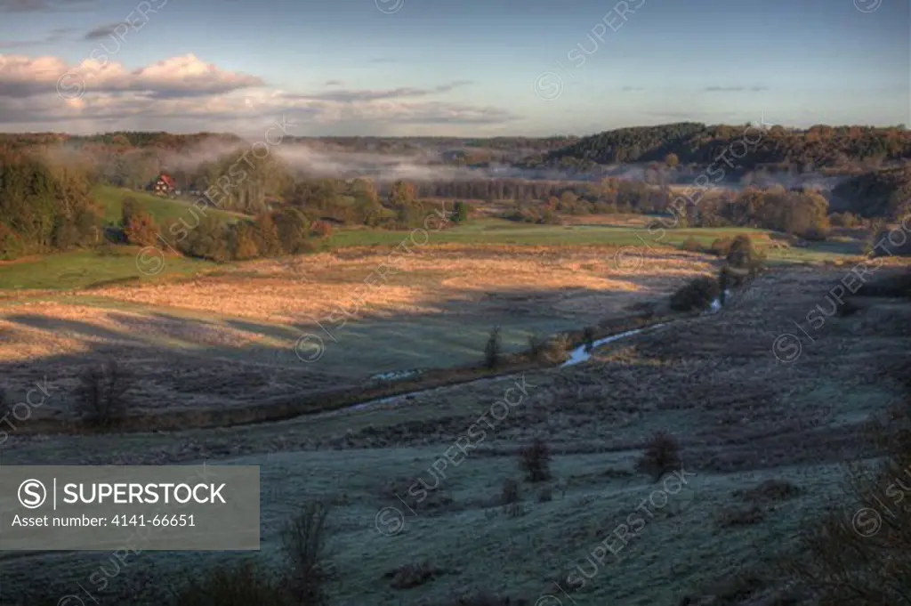 HDR image, Autumn morning with fog covering the forest in the background and a river (Vejle Aa) cutting through the frame. Photographed at Runkenbjerg in Denmark.