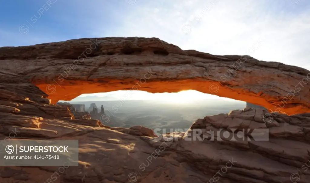 Mesa Arch with glow from sunrise light striking the canyon wall below the arch; Canyonlands National Park, Utah.