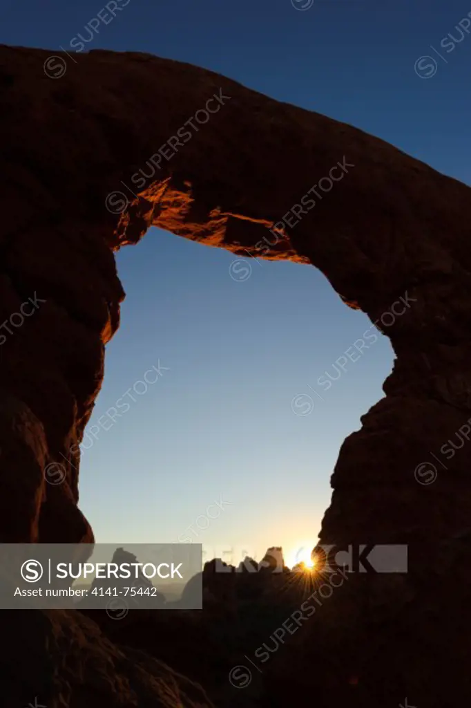 The rising sun peeks through Turret Arch; Arches National Park, Utah.