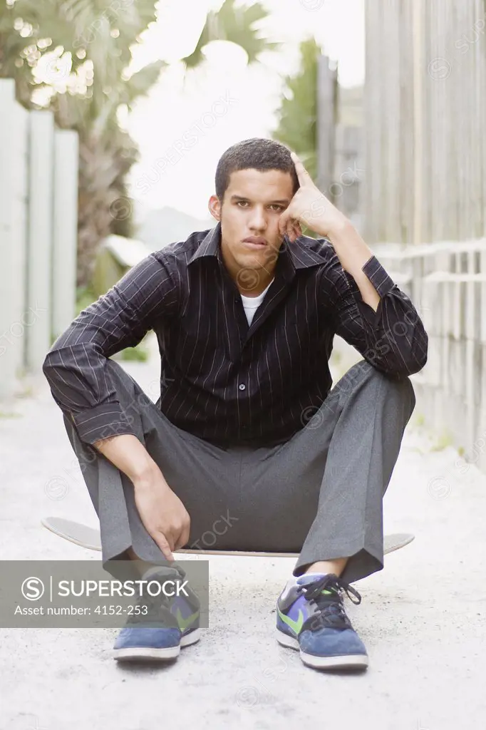 Young man sitting on a skateboard and looking sad