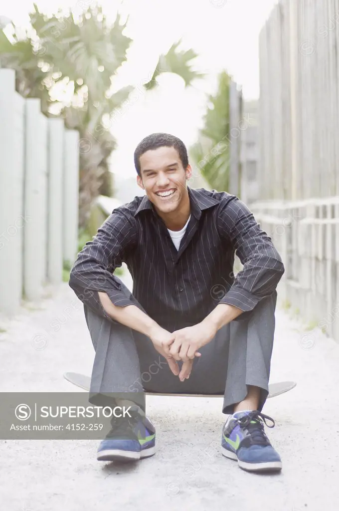 Young man sitting on a skateboard and smiling