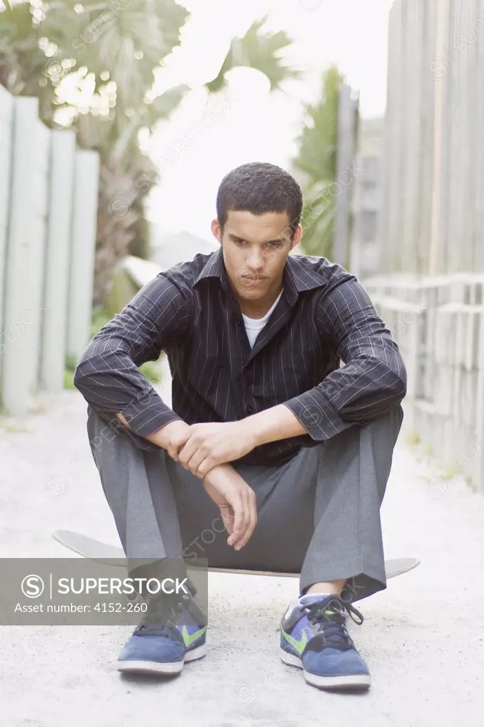 Young man sitting on a skateboard and looking sad