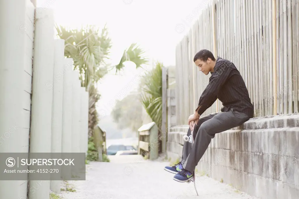 Young man sitting on a wall and holding a skateboard