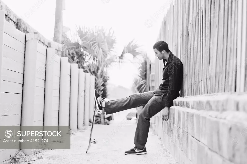 Young man sitting on a wall and playing with a skateboard