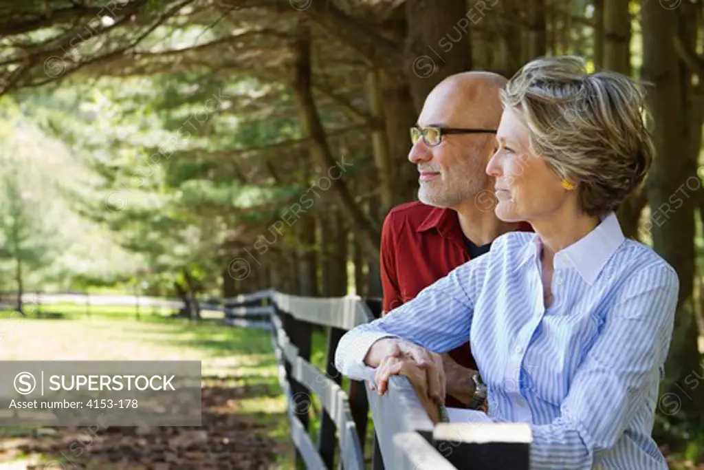 USA, Mature couple leaning on rail fence and looking at view