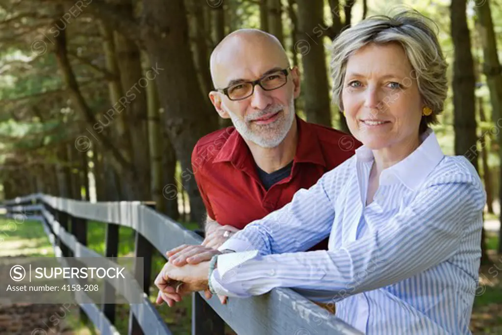 Outdoor portrait of mature couple smiling and leaning on wooden fence