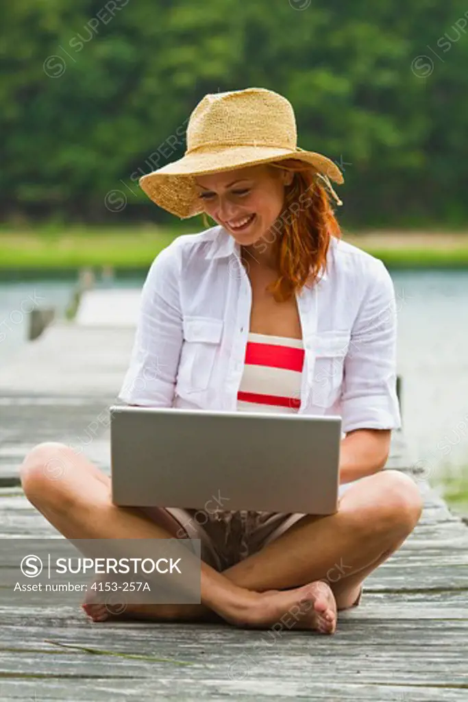 Young woman wearing straw hat using laptop on jetty