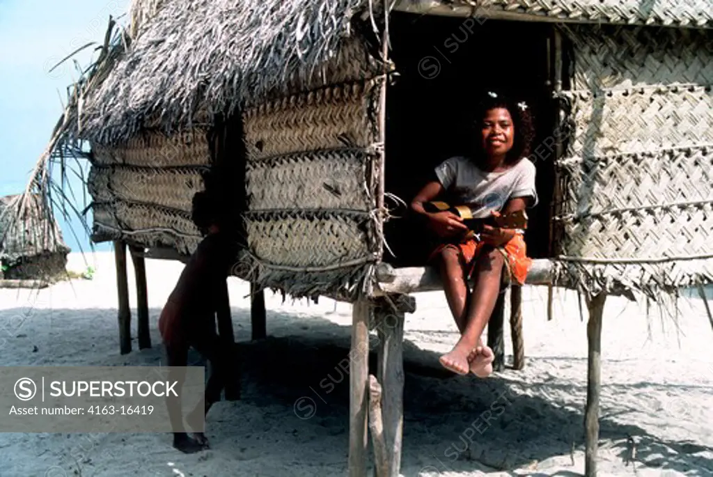PAPUA NEW GUINEA, LAUGHLAN ISLANDS, BUDALUNA ISL., GIRL PLAYING GUITAR IN HUT ON BEACH