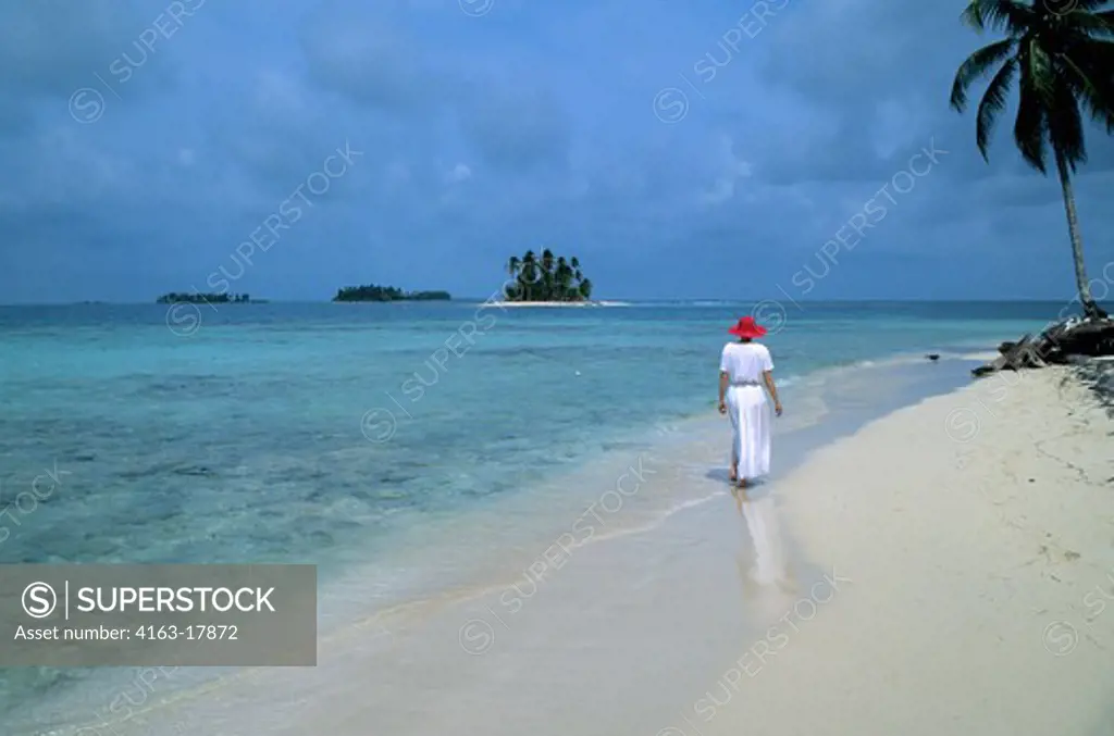 PANAMA, SAN BLAS ISLANDS, NIA TUPU ISLAND, WOMAN WITH RED HAT WALKING ON WHITE SAND BEACH