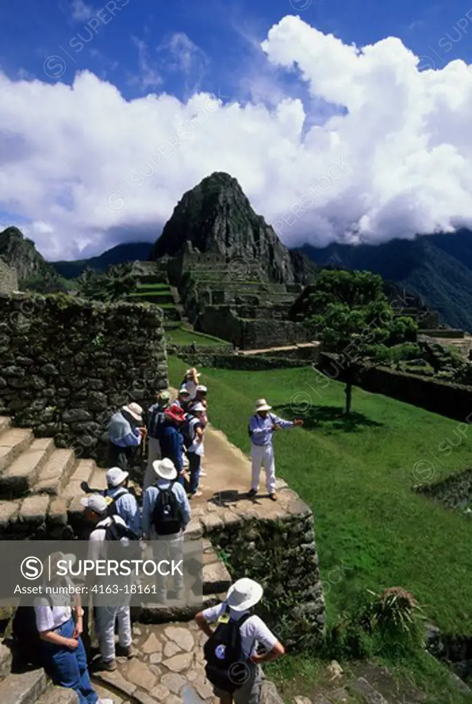 PERU, SACRED VALLEY, MACHU PICCHU, HUAYNA PICCHU IN BACKGROUND, TOURISTS LISTENING TO TOUR GUIDE