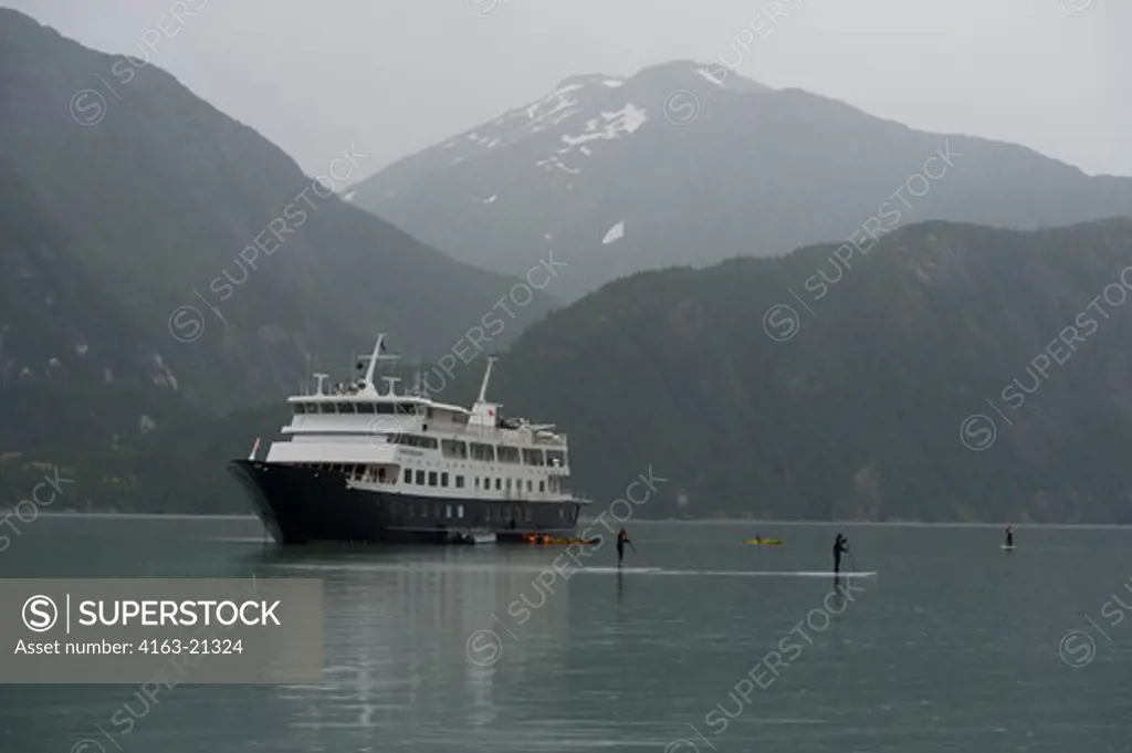 People paddleboarding at Scenery Cove, Thomas Bay, Tongass National Forest, Alaska, USA with cruise ship Safari Endeavour in background