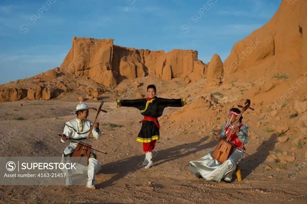 Mongolian Teenagers In Traditional Dress Performing Traditional Music And Dances With Horse Head Fiddles (Morin Khuur) At The Orange Rocks Of Bayan Zag, Commonly Known As The Flaming Cliffs In The Gobi Desert, Mongolia