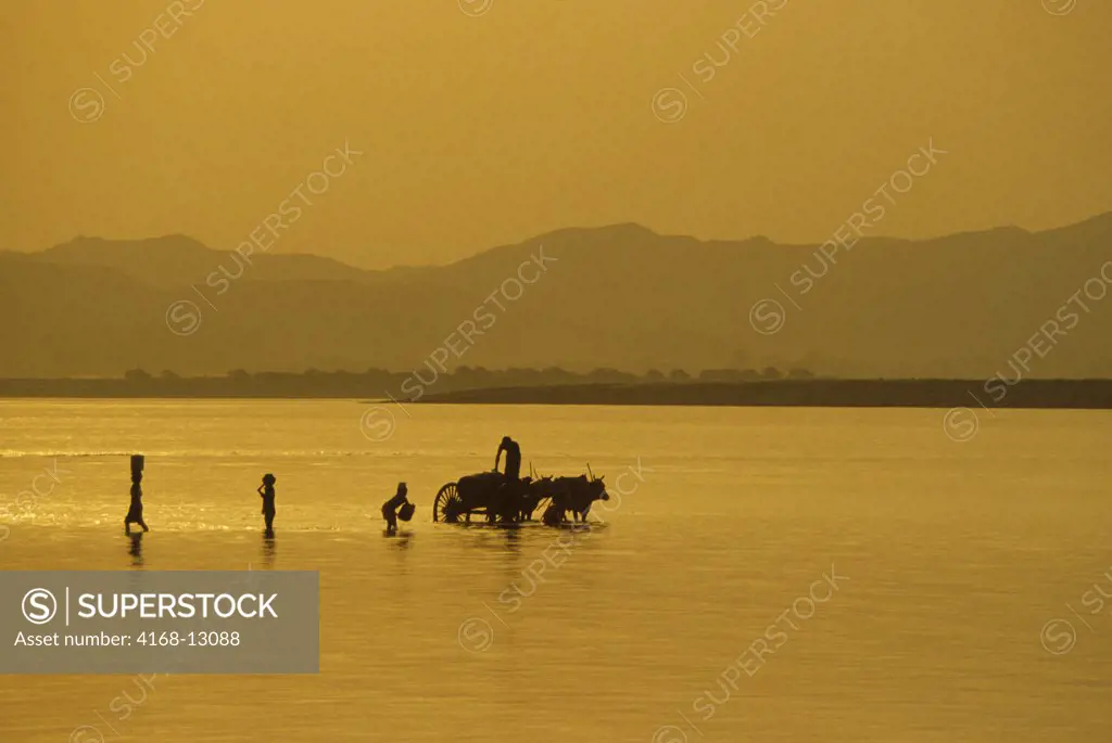 Myanmar (Burma), Pagan, Waterbearer And Ox Cart Silhoutted In The Irrawaddy River At Sunset