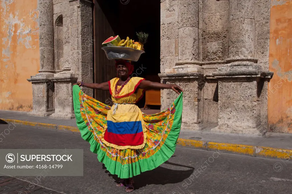 Woman With Fruits In Colonial Costume In Front Of Santo Domingo Convent On Plaza Santo Domingo In Cartagena, Colombia, A Walled City And Unesco World Heritage Site