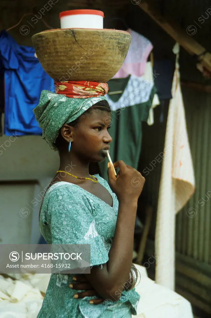 A Young Woman Carrying A Basket On Her Head At An Open Air Market In Dakar, Senegal, West Africa