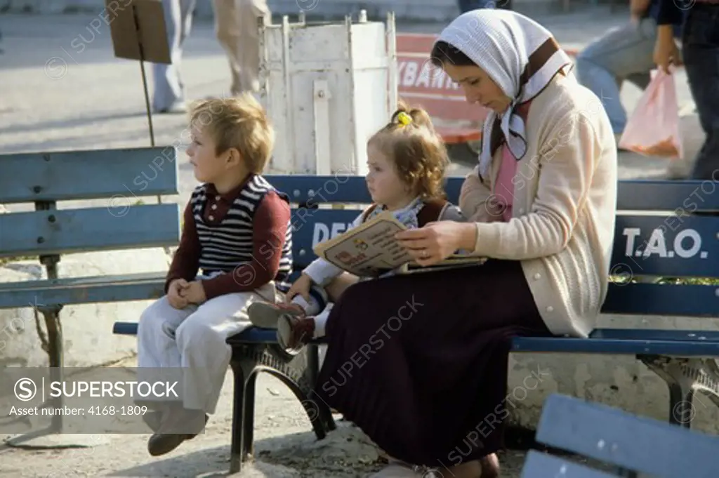 TURKEY, ISTANBUL, LOCAL WOMAN WITH CHILDREN ON BENCH READING MAGAZINE