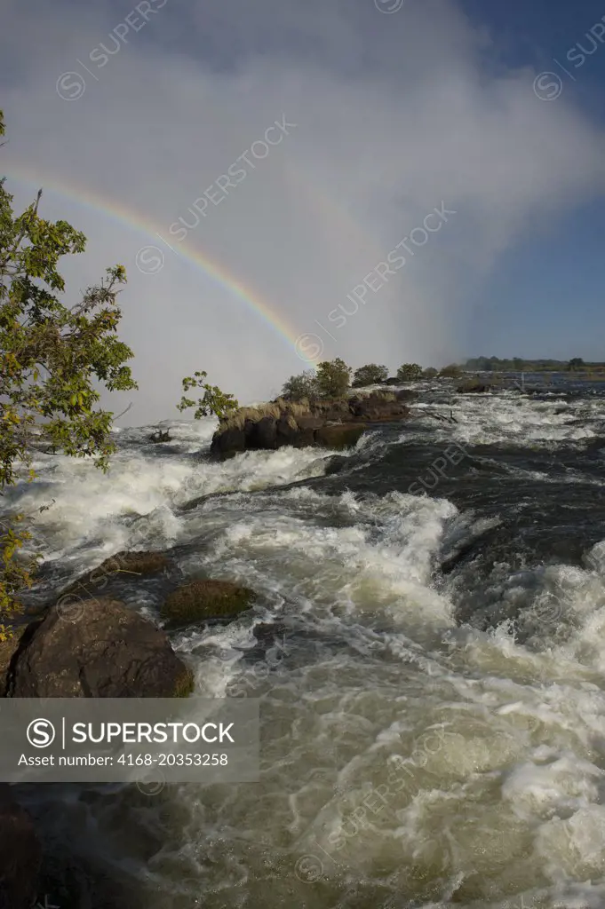 Rainbow over Victoria Falls seen from the shore of the Zambezi River at the section above the falls near Livingston in Zambia.