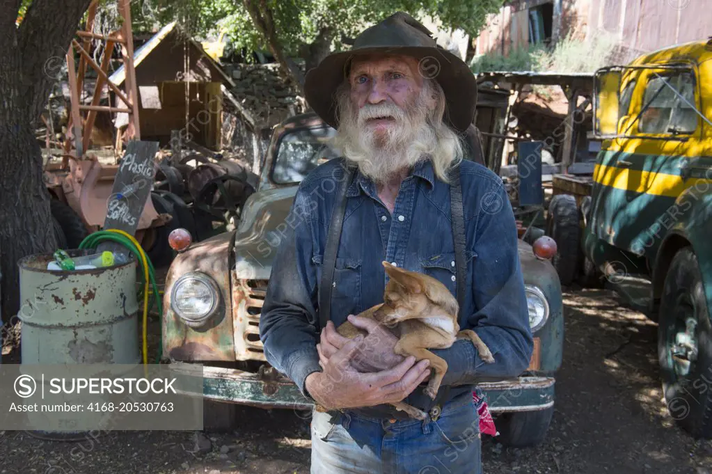 Portrait of Don Robertson, the owner and founder of the historic Gold King Mine and Ghost Town from the 1890s outside of Jerome in Arizona, USA with his A Chihuahua dog (Chiwawa dog).
