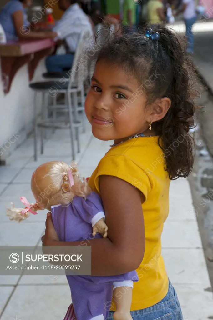 A portrait of a girl holding a doll at the bus station in the town of Upala in Costa Rica.