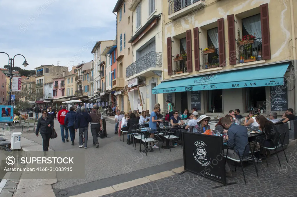 People in outdoor restaurants at the port in Cassis, which is a picturesque seaside community, located 20 km east of Marseille in the Provence-Alpes-Côte d'Azur region in southern France.