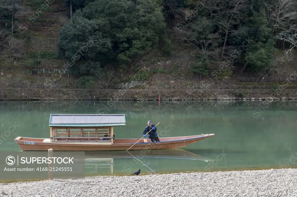 A man is poling a boat on the Katsura River in Kyoto, Japan.