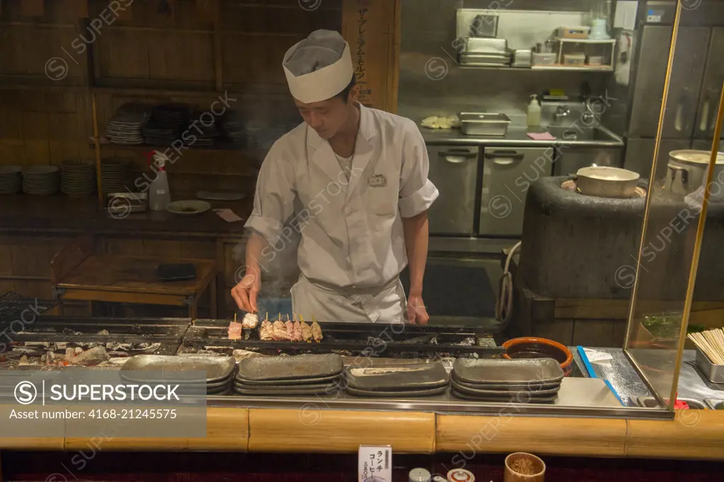 A chef is cooking chicken skewers in a restaurant in Kyoto, Japan.