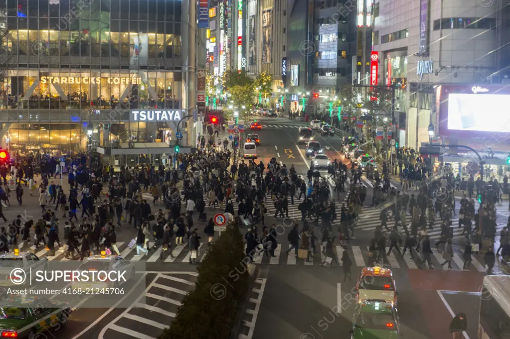 View at night of the intersection outside Shibuya Station with pedestrians crossing from all sides in Tokyo, Japan.