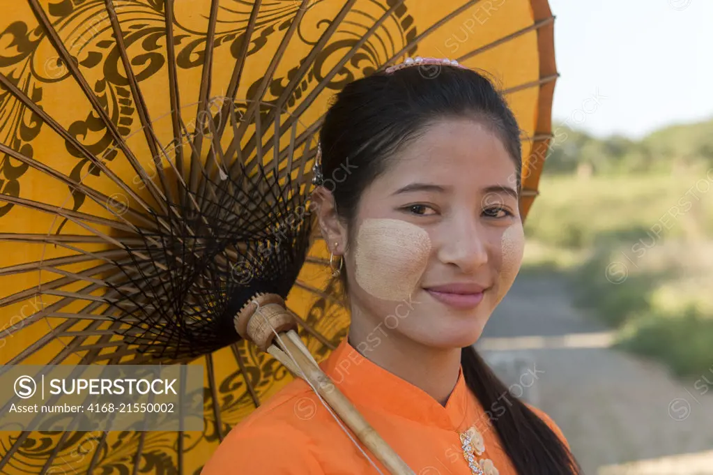 Close-up of a young woman (model) in traditional dress holding a parasol at a small temple complex in Bagan, Myanmar.