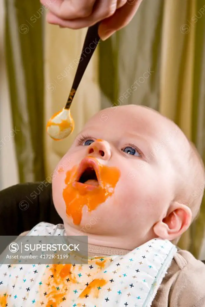 Messy hungry baby eating solid food from spoon