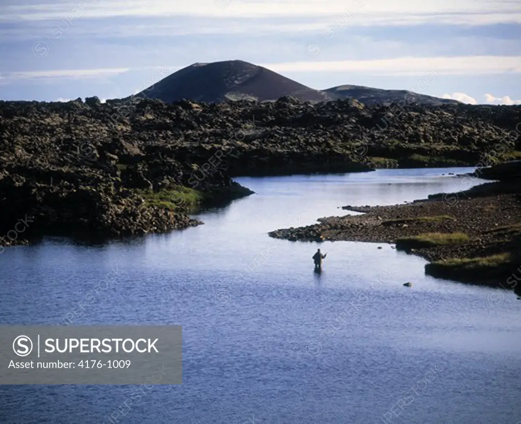 Man fishing in river ( Haffjardara ) below mountain peak. Iceland