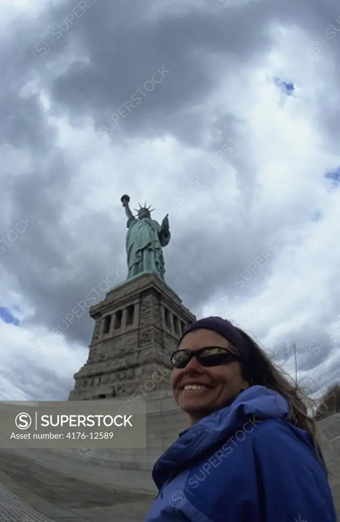 Low angle view of the Statue of Liberty against cloudy sky and a woman in the foreground