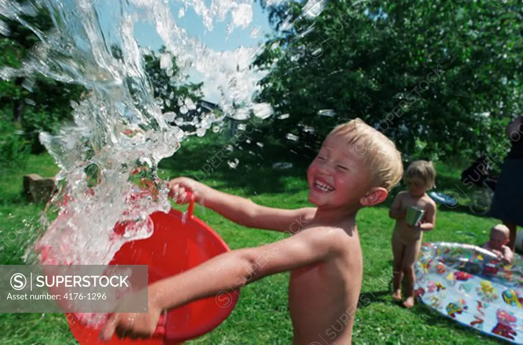 Boy splashing out water from a bucket and smiling, Sweden