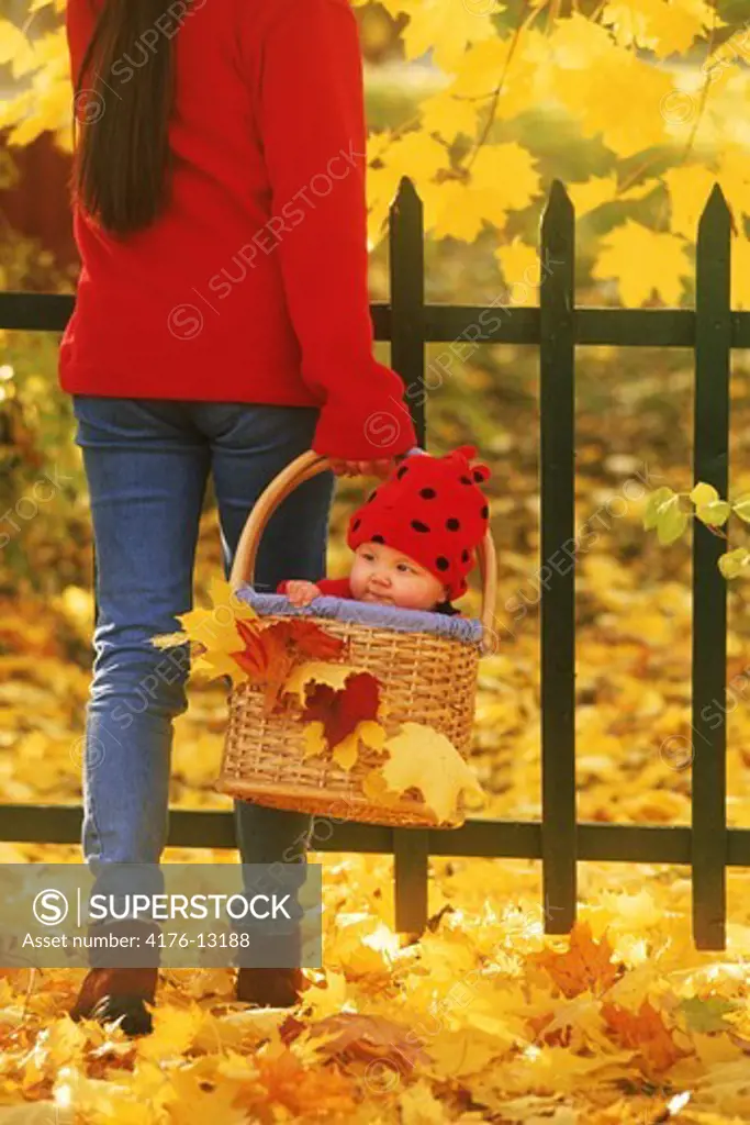 Mother carrying baby in basket amid autumn colors