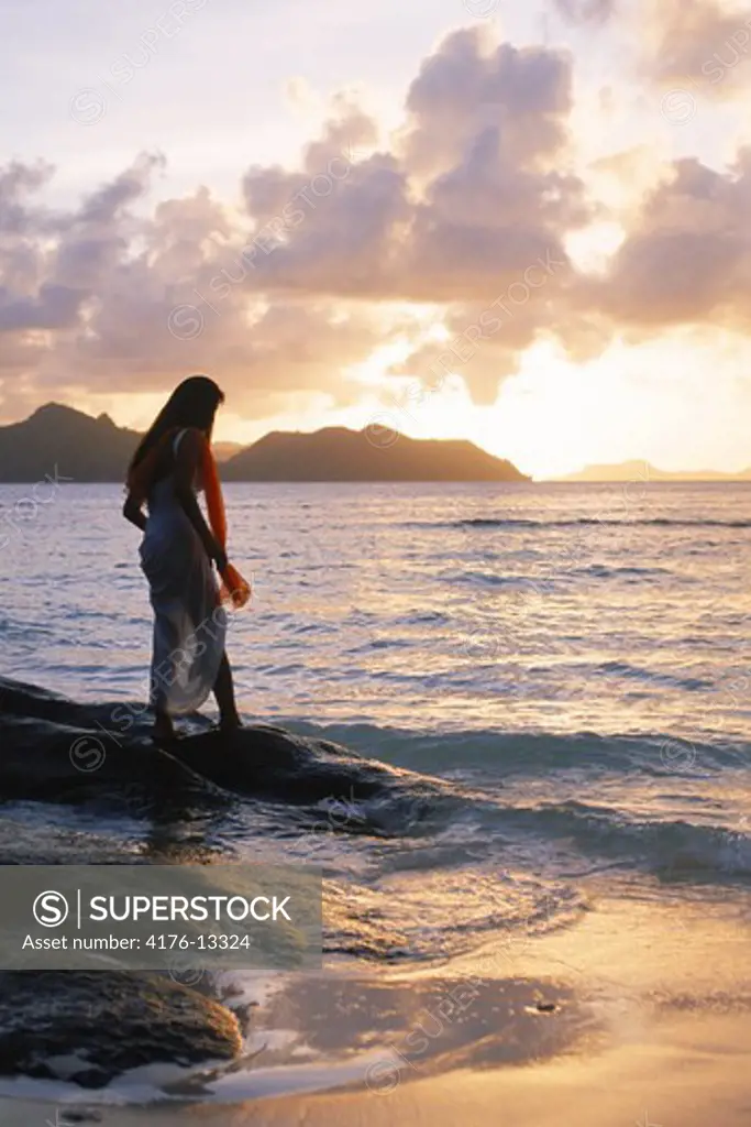 Woman in long white dress alone at sunset on La Digue Island