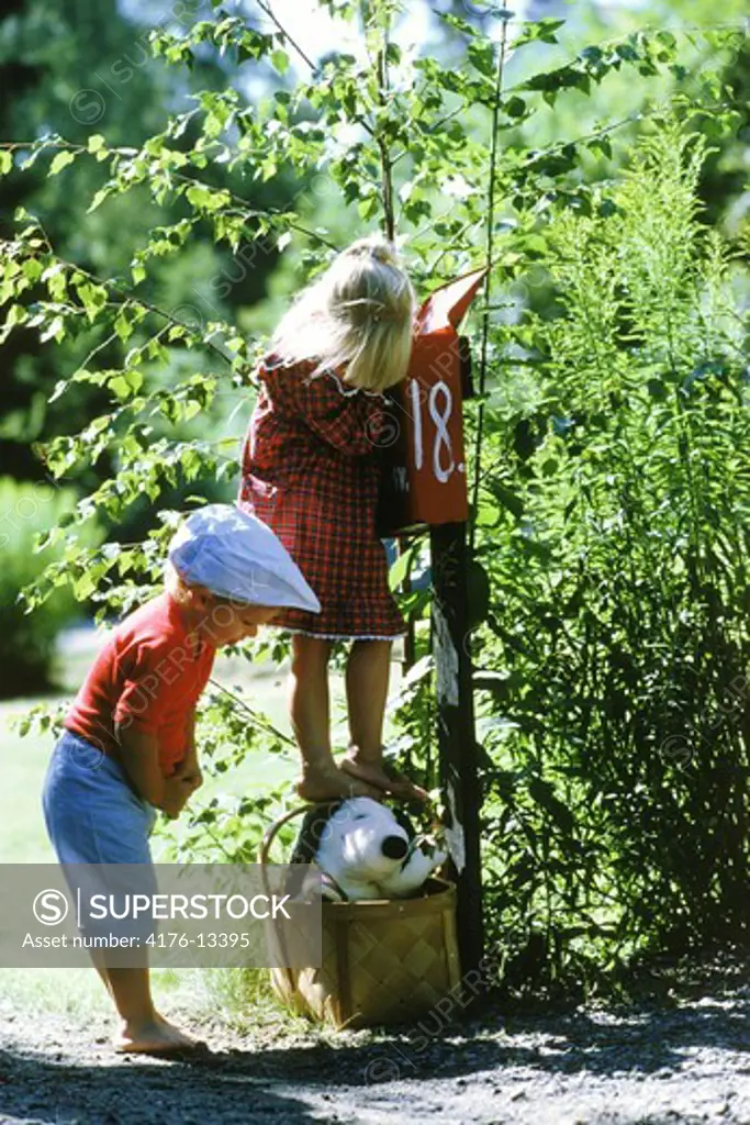 Boy and girl and snoopy in a basket at rural mailbox on summer day in Sweden