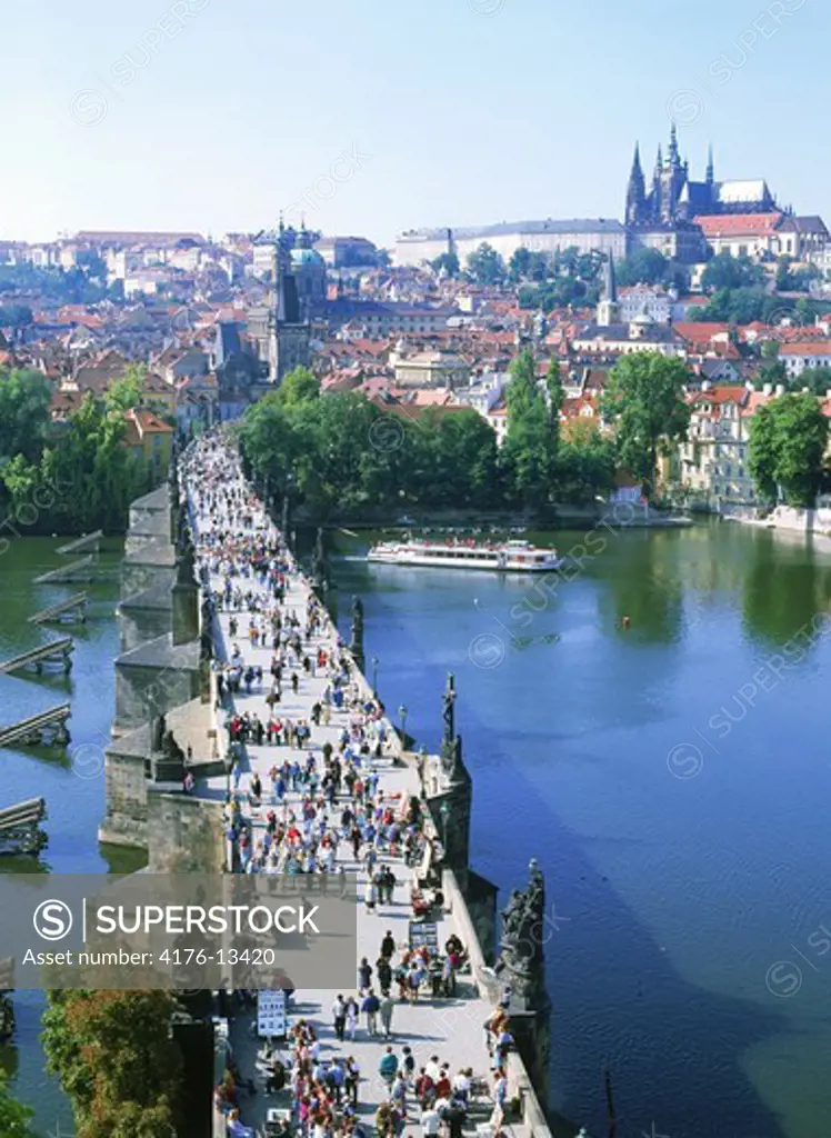 People crossing Charles Bridge over Vltava River with Hrdcany Castle and St. Vitus Cathedral