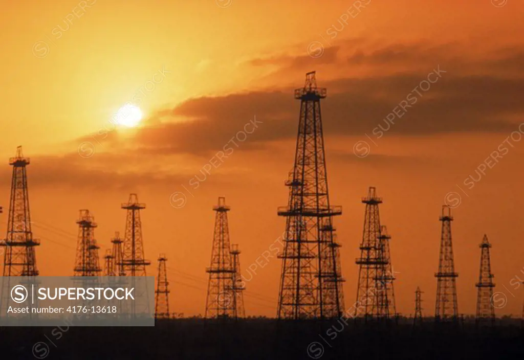 Oil derricks silhouetted against sunset skies