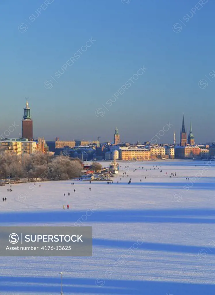 People walking across middle of Stockholm in winter on frozen Riddarfjarden waterway with City Hall on left