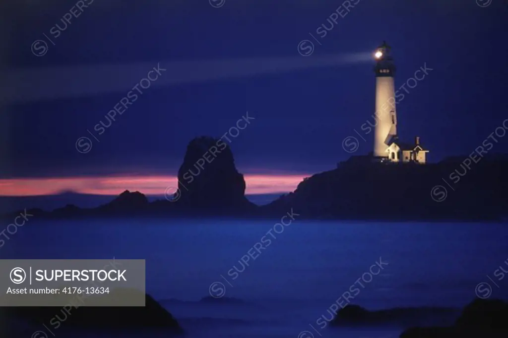 Pigeon Point Lighthouse on rocky ledge over Pacific Ocean in California at dusk