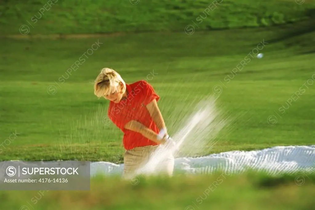 Woman golfer blasting out of sand trap or bunker