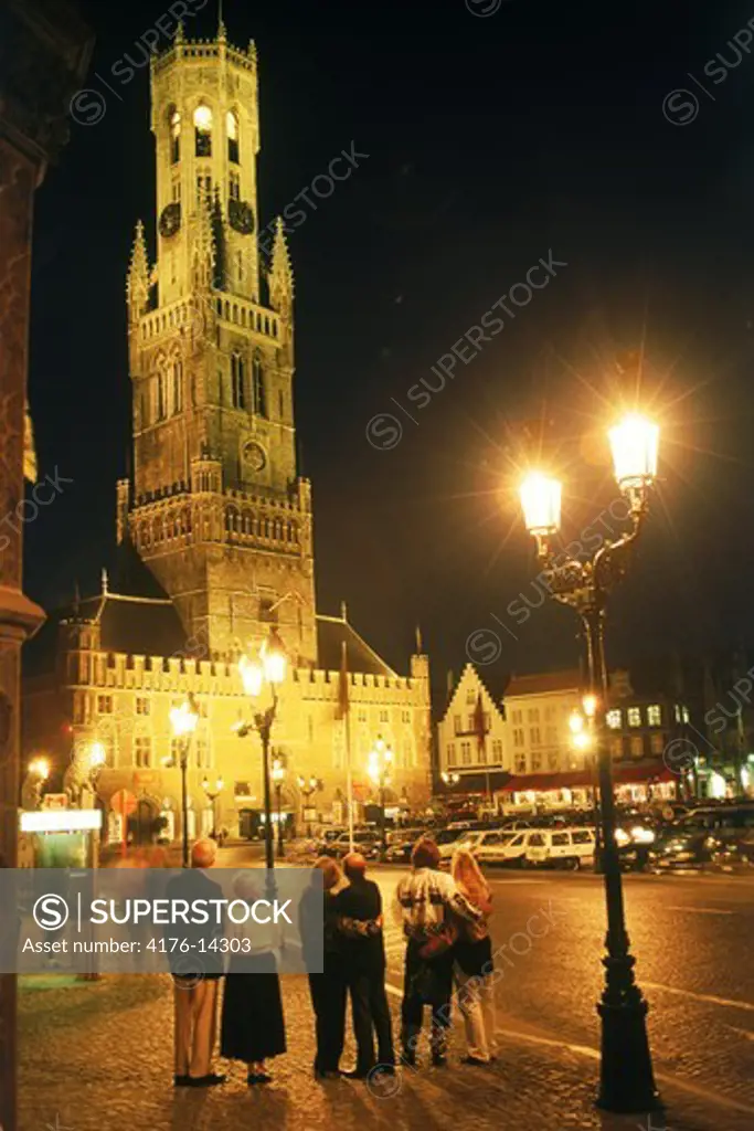 Market Square in Brugge with tourists, lamplights and Cathedral belfry at night