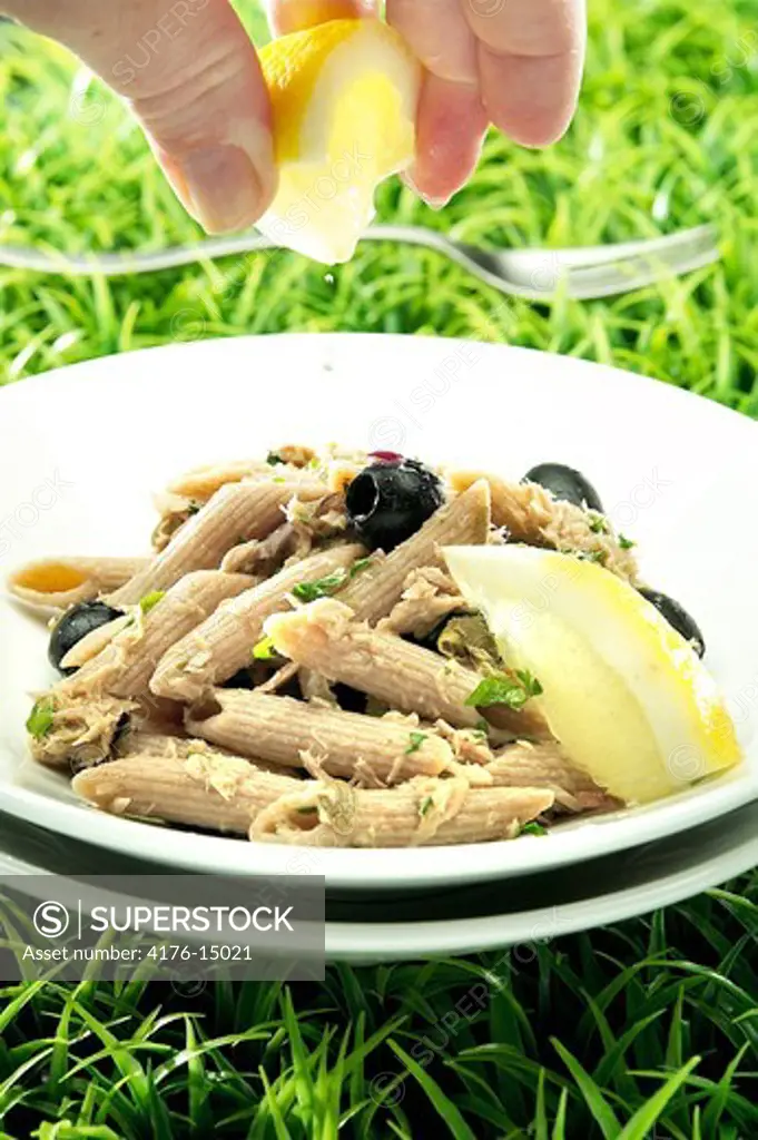 A hand squeezing lemon over a pasta dish on grass