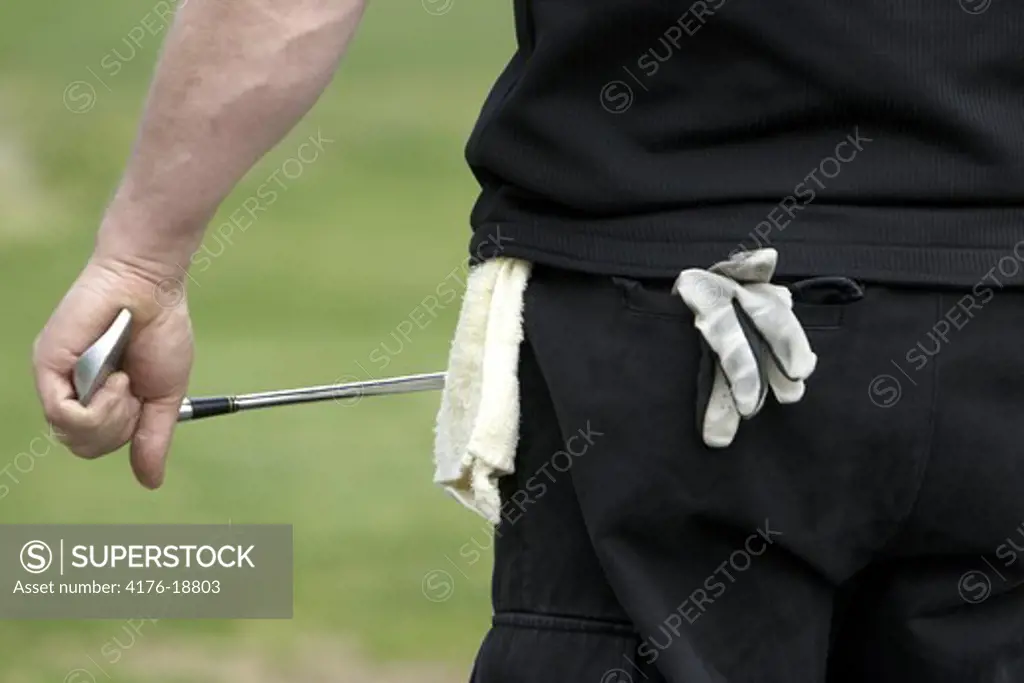 Rear view of a golfer holding golf club with glove and towel hanging out of back pocket